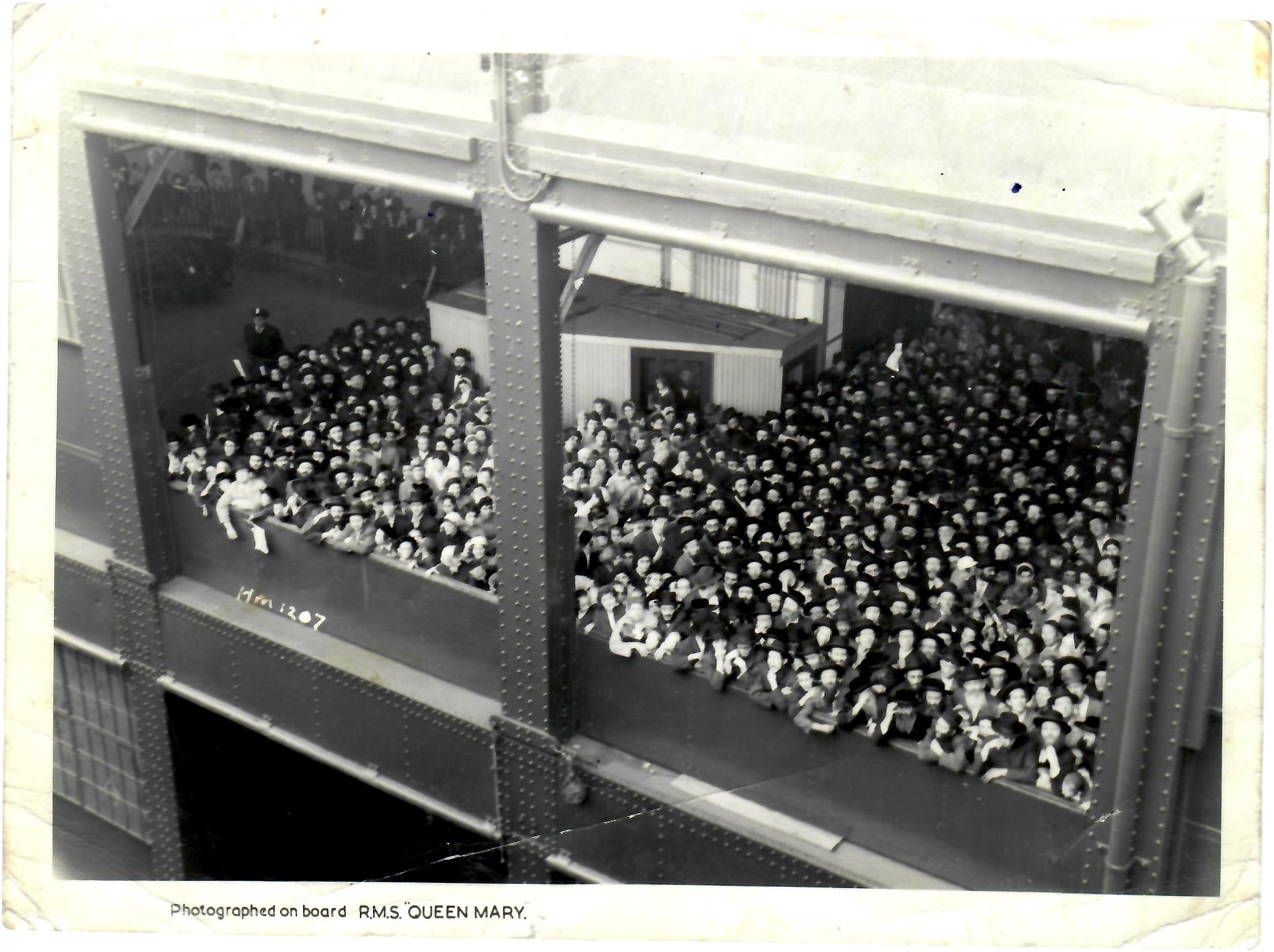 Photograph taken from the deck of the Queen Mary, looking down on a crowd waiting under the pier shed