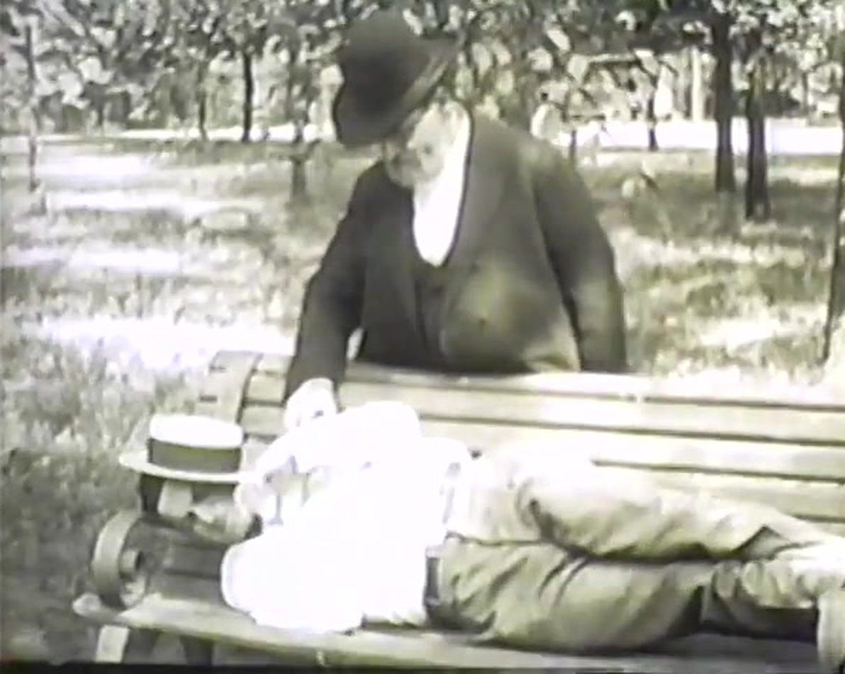 A young man asleep on a park bench while Rabbi Sivitz stands behind him