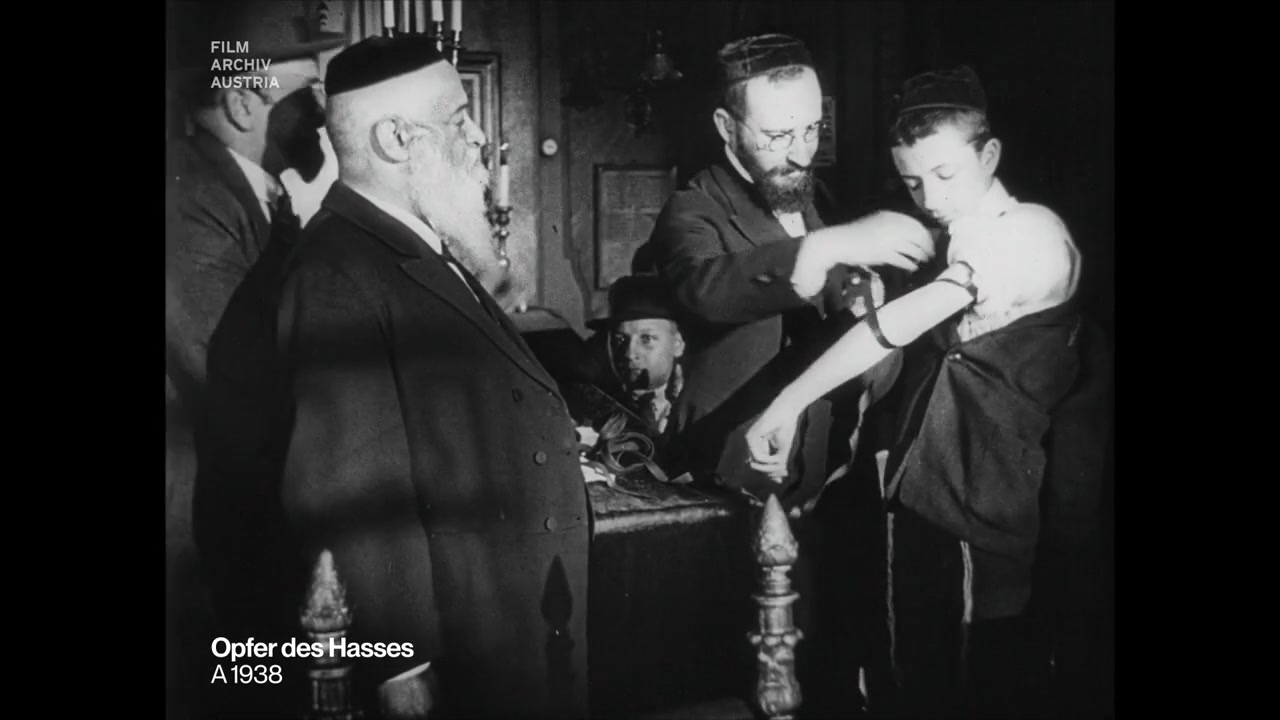 Rabbi Yeshaya Furst watches a boy put on tefillin at a bar mitzvah, 1923